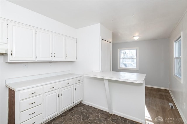 kitchen with baseboards, a peninsula, light countertops, and white cabinetry