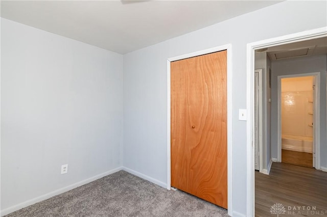 unfurnished bedroom featuring a closet, baseboards, carpet floors, and attic access