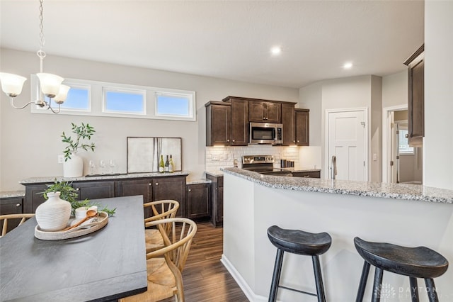 kitchen with hanging light fixtures, light stone countertops, appliances with stainless steel finishes, dark hardwood / wood-style flooring, and a chandelier