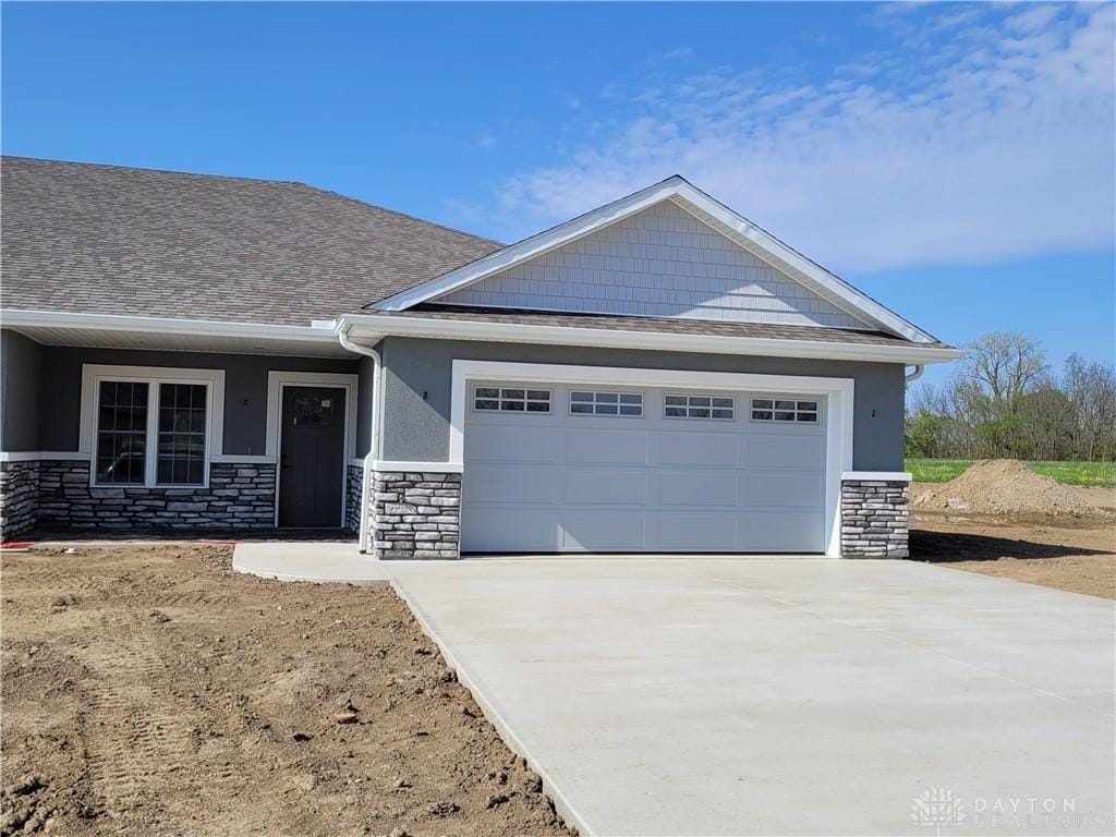 craftsman-style house featuring an attached garage, driveway, stone siding, and stucco siding
