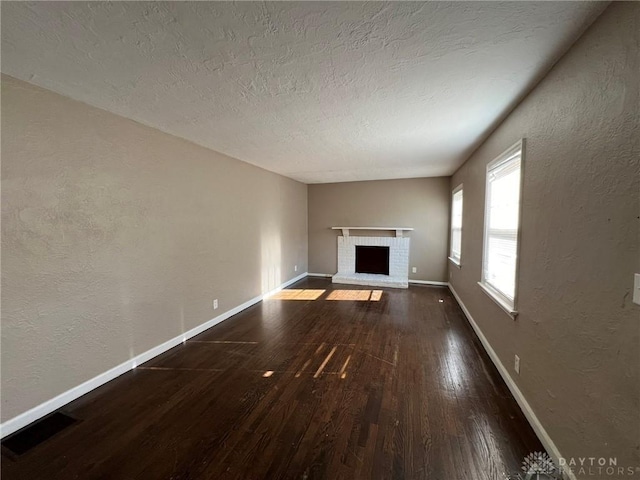 unfurnished living room featuring a textured ceiling, dark hardwood / wood-style floors, and a brick fireplace