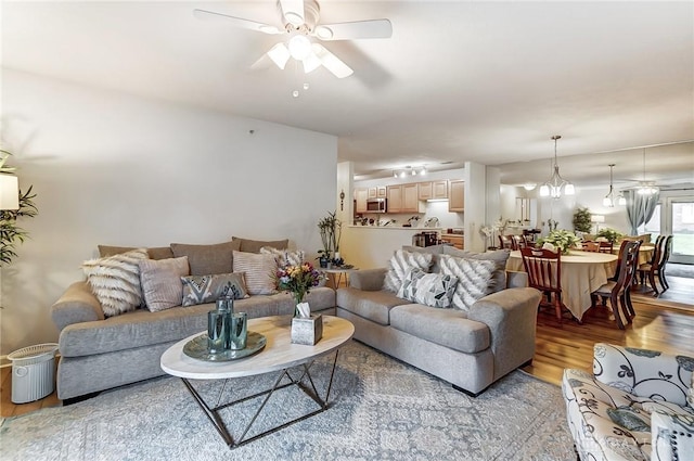 living room with ceiling fan with notable chandelier and light hardwood / wood-style flooring