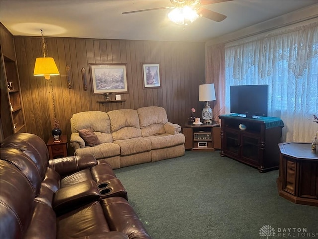 living room with ceiling fan, wooden walls, and dark colored carpet