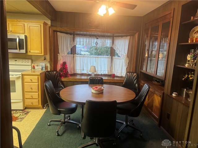 carpeted dining room with ceiling fan and wooden walls