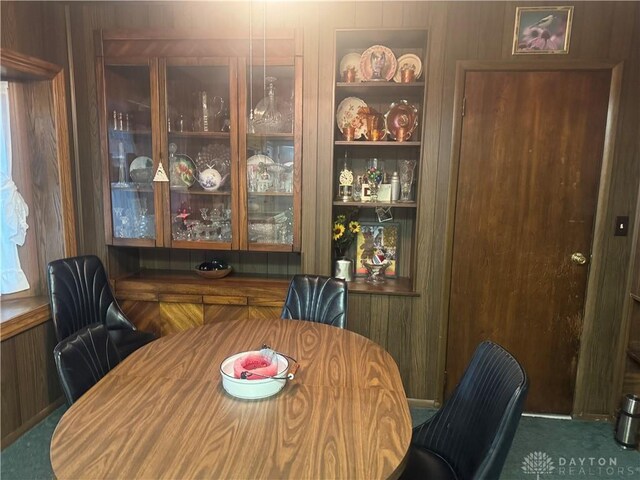 carpeted dining space featuring wood walls