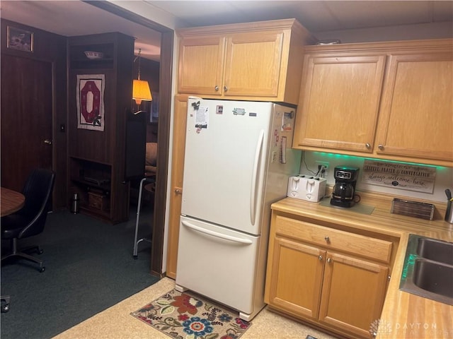 kitchen featuring sink, light brown cabinets, hanging light fixtures, wood counters, and white fridge