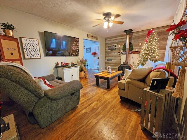 living room featuring wood walls, ceiling fan, light hardwood / wood-style floors, and a textured ceiling