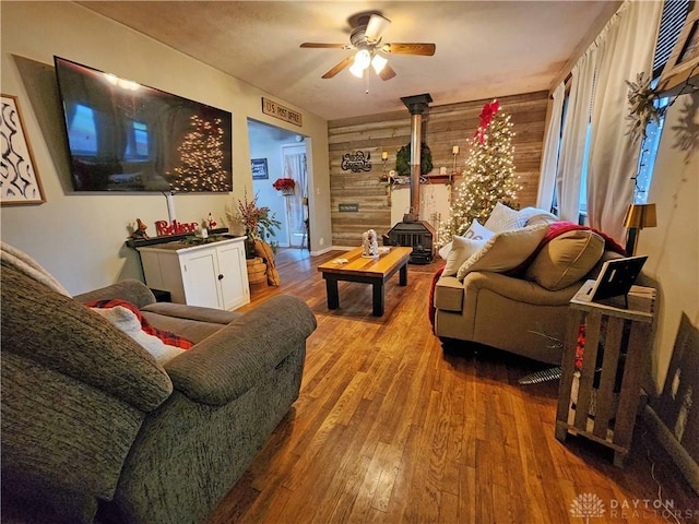 living room with hardwood / wood-style floors, ceiling fan, wood walls, and a wood stove