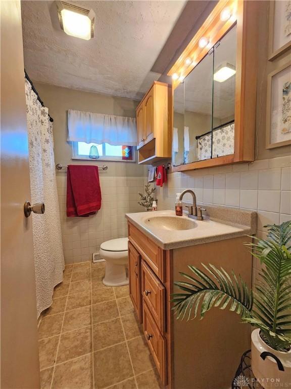 bathroom featuring vanity, tile patterned floors, toilet, tile walls, and a textured ceiling