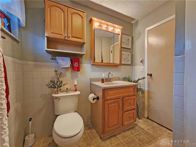 bathroom with toilet, tile walls, a textured ceiling, vanity, and tile patterned flooring