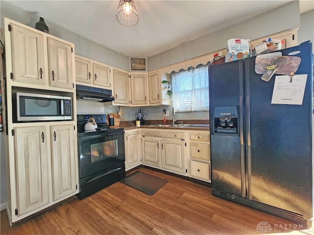 kitchen with sink, cream cabinets, black appliances, and light hardwood / wood-style floors