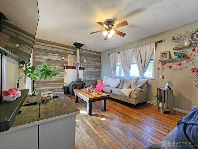 living room with hardwood / wood-style floors, wooden walls, a wood stove, ceiling fan, and a textured ceiling