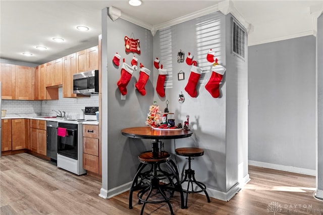 kitchen featuring appliances with stainless steel finishes, tasteful backsplash, light hardwood / wood-style flooring, and crown molding