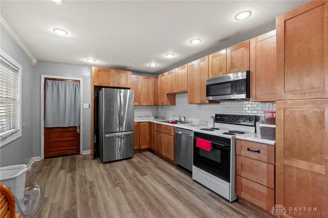 kitchen featuring appliances with stainless steel finishes, light wood-type flooring, backsplash, crown molding, and sink