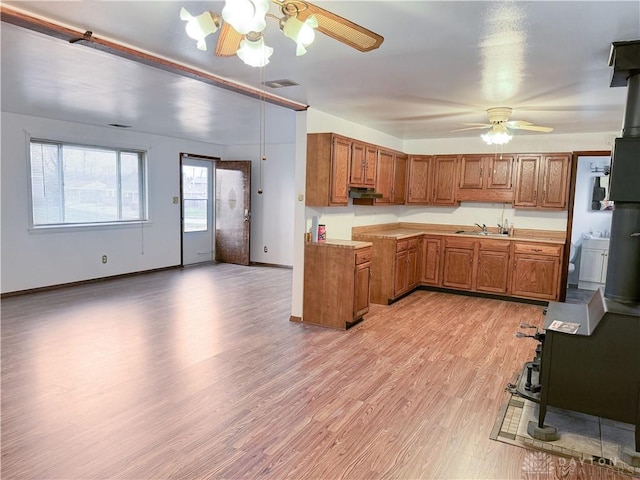 kitchen with a wood stove, ceiling fan, sink, and light wood-type flooring