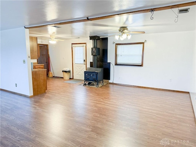 unfurnished living room featuring a wood stove, ceiling fan, and light hardwood / wood-style flooring