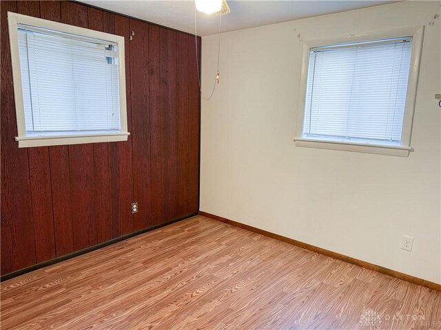 empty room with wooden walls, ceiling fan, and light wood-type flooring