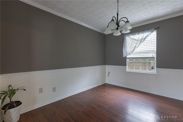 empty room featuring dark wood-style flooring, crown molding, an inviting chandelier, wainscoting, and a textured ceiling