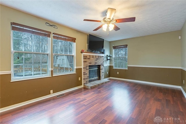 unfurnished living room with a textured ceiling, dark wood-type flooring, a brick fireplace, and a healthy amount of sunlight