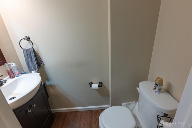 half bathroom with toilet, baseboards, wood finished floors, and vanity