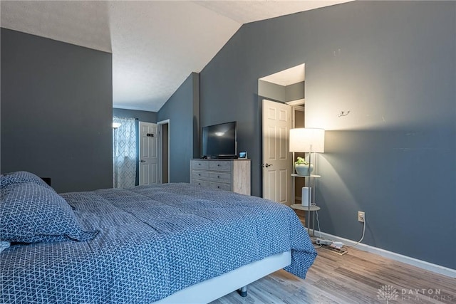 bedroom with vaulted ceiling, baseboards, and wood finished floors