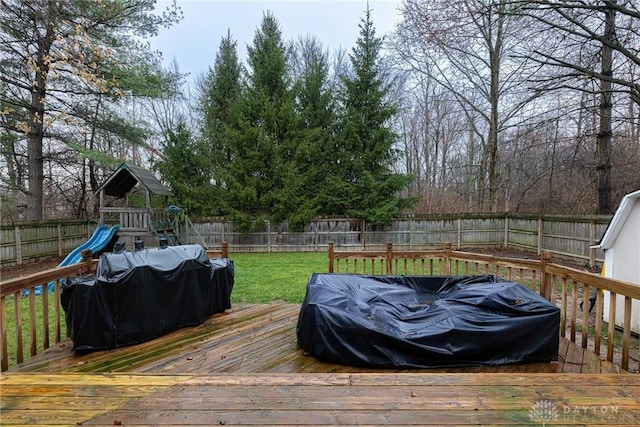 wooden terrace with grilling area, a playground, a fenced backyard, and a lawn