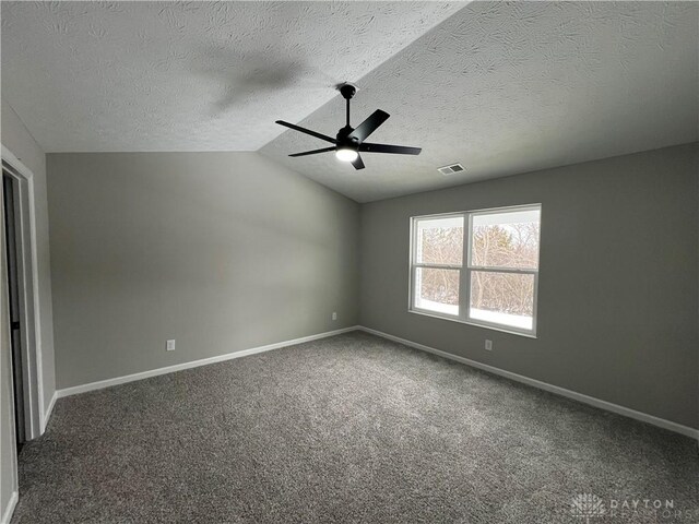 carpeted empty room featuring vaulted ceiling, ceiling fan, and a textured ceiling