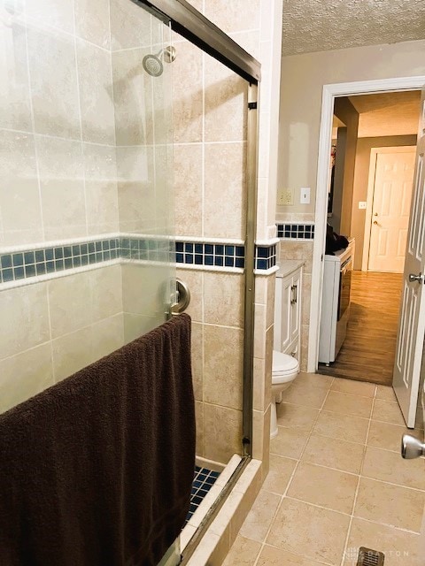 bathroom with tile patterned flooring, toilet, a textured ceiling, tile walls, and walk in shower