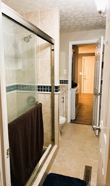 bathroom with tile patterned flooring, a textured ceiling, an enclosed shower, toilet, and tile walls