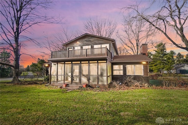 rear view of house featuring a chimney, a sunroom, a lawn, and a balcony