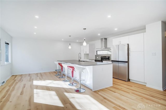 kitchen featuring an island with sink, wall chimney range hood, a breakfast bar, stainless steel appliances, and light wood finished floors