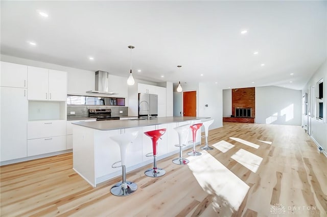 kitchen featuring wall chimney range hood, light wood finished floors, modern cabinets, and stainless steel range with electric cooktop