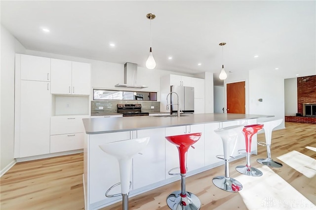 kitchen with electric range, a sink, wall chimney range hood, and light wood-style floors