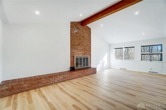 unfurnished living room with visible vents, beamed ceiling, a brick fireplace, and wood finished floors