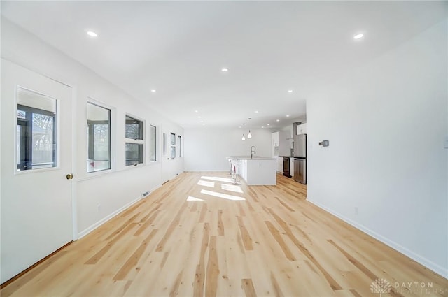 unfurnished living room with recessed lighting, light wood-style flooring, baseboards, and a sink