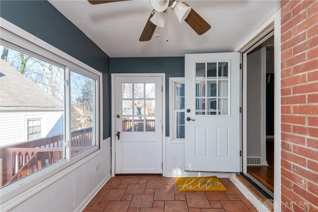 doorway to outside featuring ceiling fan and brick wall