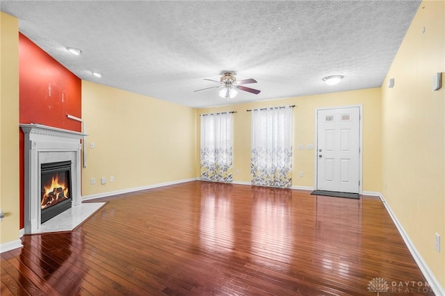 unfurnished living room with ceiling fan, a fireplace, wood-type flooring, and a textured ceiling