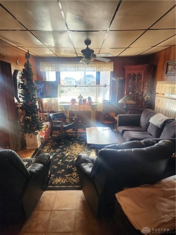 living room with light tile patterned floors, ceiling fan, and wood walls