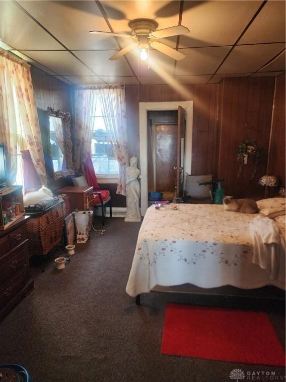 bedroom with dark colored carpet, ceiling fan, and wooden walls