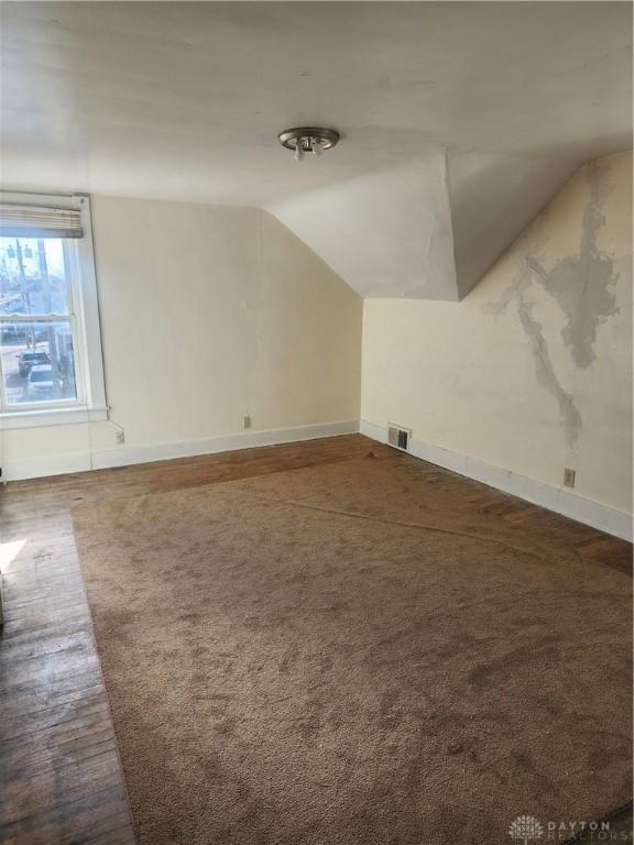 bonus room with lofted ceiling and dark colored carpet