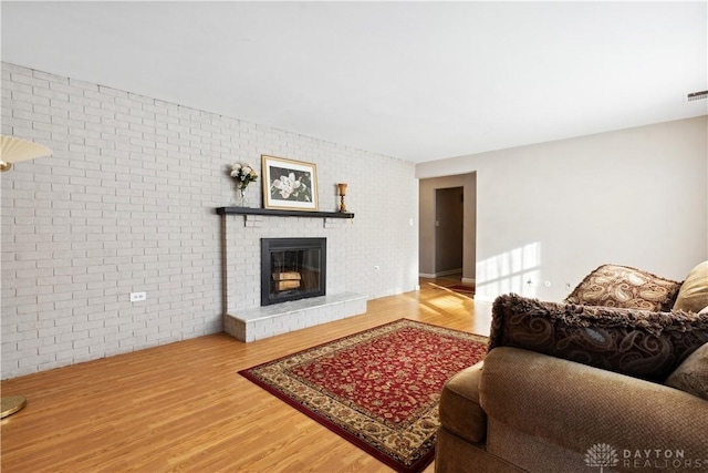 living room with a fireplace, brick wall, and hardwood / wood-style flooring