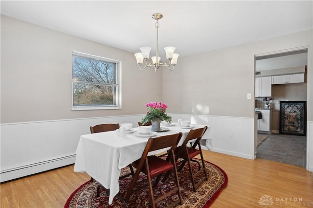 dining area with light hardwood / wood-style floors, baseboard heating, and an inviting chandelier