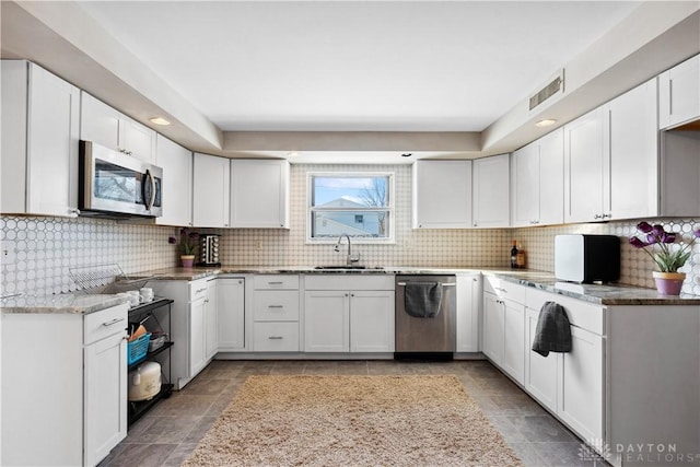 kitchen with tasteful backsplash, sink, white cabinets, and appliances with stainless steel finishes