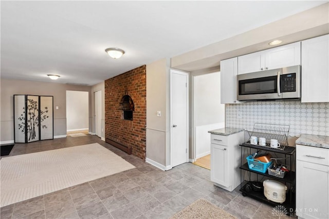 kitchen with light stone countertops, white cabinetry, brick wall, and tasteful backsplash