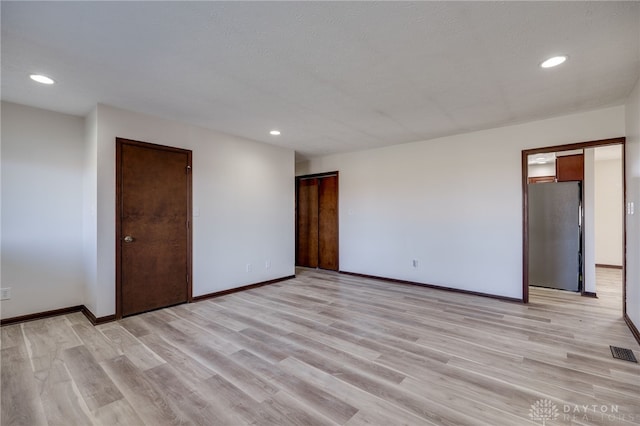 unfurnished bedroom with light wood-type flooring, a textured ceiling, and stainless steel refrigerator