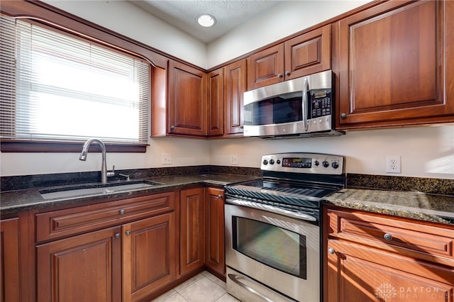 kitchen featuring light tile patterned flooring, appliances with stainless steel finishes, dark stone counters, and sink