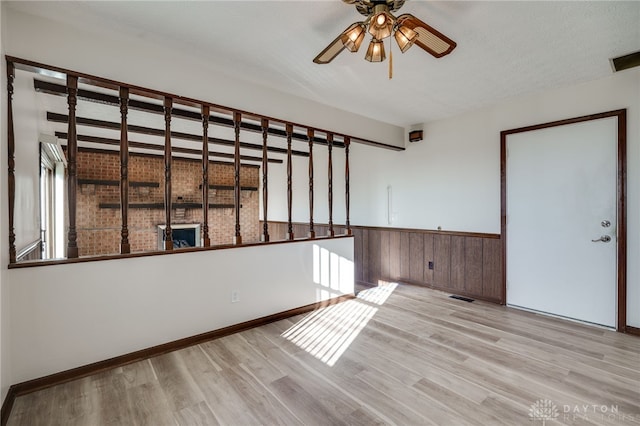 unfurnished room with a textured ceiling, light wood-type flooring, ceiling fan, and wooden walls