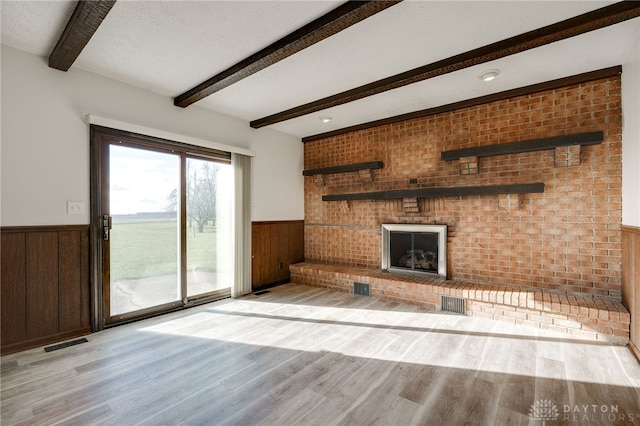 unfurnished living room featuring beam ceiling, light hardwood / wood-style flooring, and brick wall