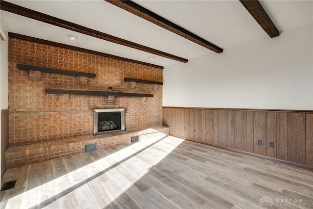 unfurnished living room featuring wood walls, beam ceiling, brick wall, and light hardwood / wood-style flooring