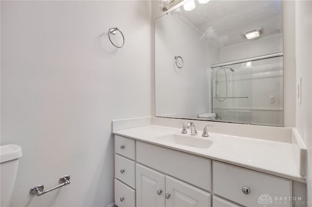 bathroom featuring a textured ceiling, toilet, vanity, a shower with shower door, and ornamental molding